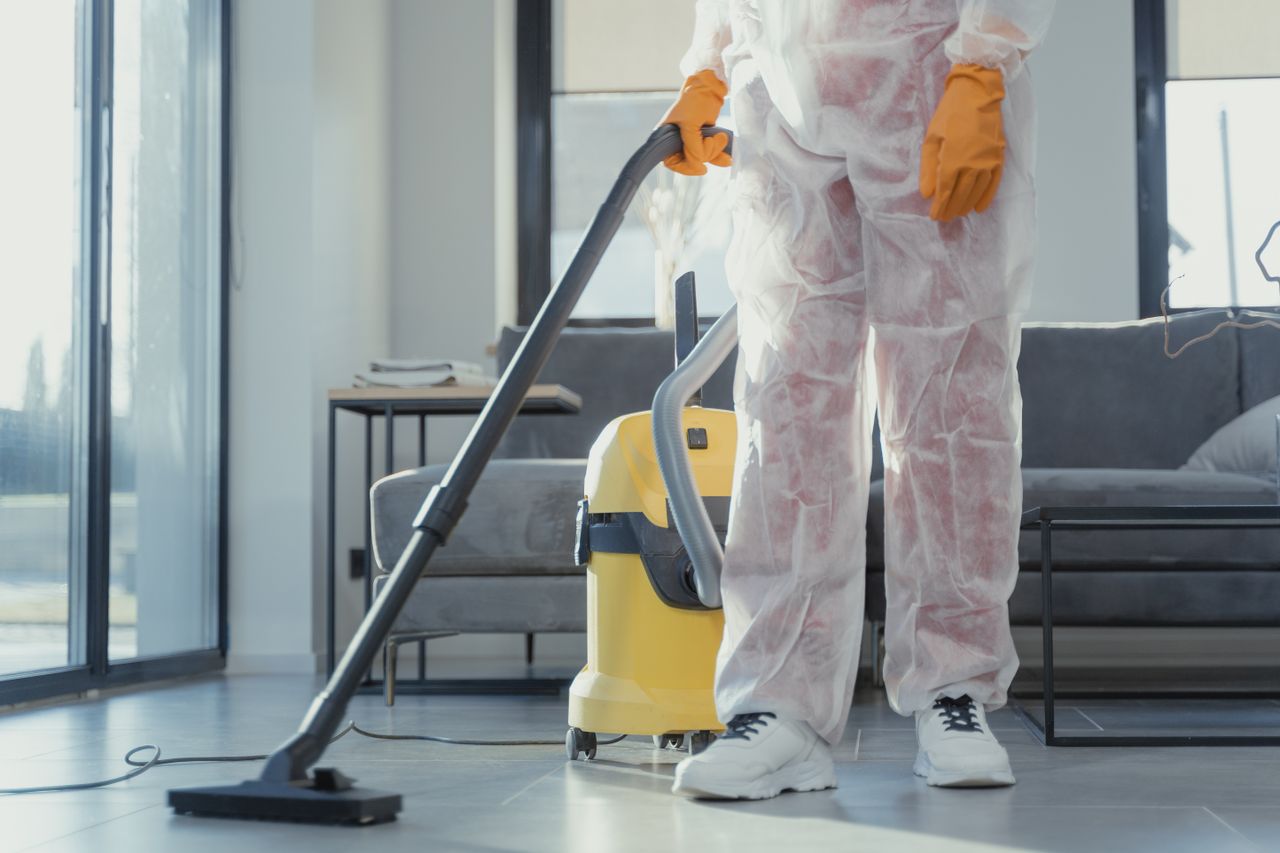 creative-03 A cleaner in protective coveralls and gloves vacuuming a modern living room.