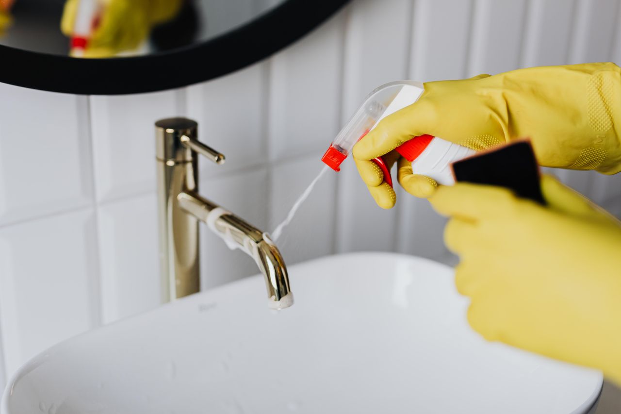mobile-01 From above anonymous housekeeper in yellow rubber gloves spraying cleaner to chrome water faucet in bathroom